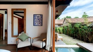 Una stanza con pavimento in legno, un letto, una sedia, un'opera d'arte incorniciata e vista su piscina e giardino.