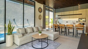 A modern living room with a sofa, coffee table, and large windows overlooking a pool.