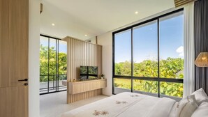 A modern bedroom with a large bed, a TV on a wooden console, and a balcony with a view of greenery.