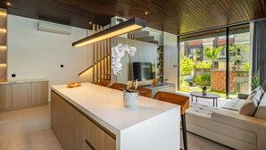 A modern kitchen with a central island, wooden cabinets, and a dining area with a sofa and table.