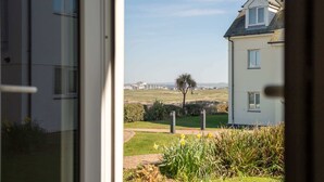 A view from inside a house looking out to a grassy field with a building in the distance. - Stylish Apartment, Garden with Beautiful Sea Views (Newquay)