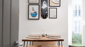 A dining area with a wooden table and chairs, framed artwork on the wall, and a view of the outside. - Stylish Apartment, Garden with Beautiful Sea Views (Newquay)