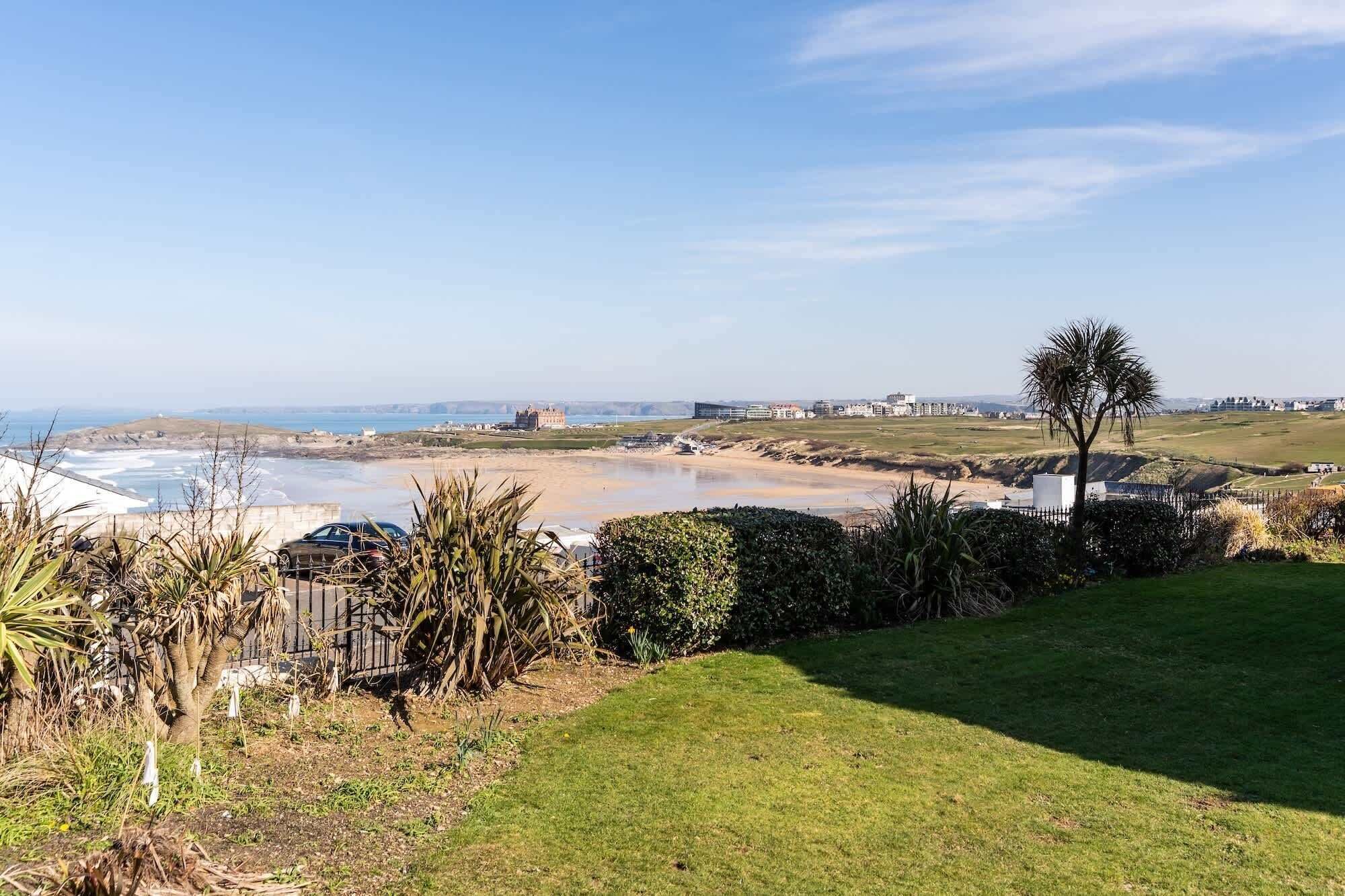 A coastal landscape with a beach, grassy areas, and a few buildings in the distance.