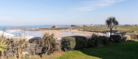 A coastal landscape with a beach, grassy areas, and a few buildings in the distance.