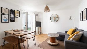 A modern living room with a dining area, a grey sofa with yellow cushions, a round coffee table, and a TV in the background. - Stylish Apartment, Garden with Beautiful Sea Views (Newquay)