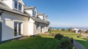 A coastal house with a large lawn, a satellite dish, and a view of the sea. - Stylish Apartment, Garden with Beautiful Sea Views (Newquay)