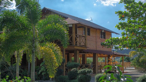 Una casa de madera con balcón, rodeada de exuberante vegetación y un jardín cuidado.