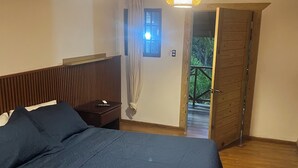 Un dormitorio con cabecera de madera, cama con colcha azul oscuro, dos lámparas colgantes y una ventana con cortinas.