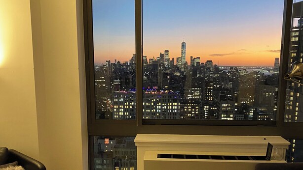 Un salon moderne doté d’une grande fenêtre donnant sur une vue panoramique de la ville au crépuscule.