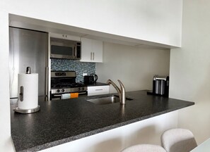 A modern kitchen with a stainless steel refrigerator, a microwave, a stove, and a sink with a faucet. - Manhattan Lux High-Rise next to Empire State Bldg (New York)
