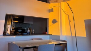 Une cuisine moderne équipée d’un four à micro-ondes, d’une bouilloire et d’une machine à café. On y trouve une table à manger avec quatre chaises et un lampadaire.