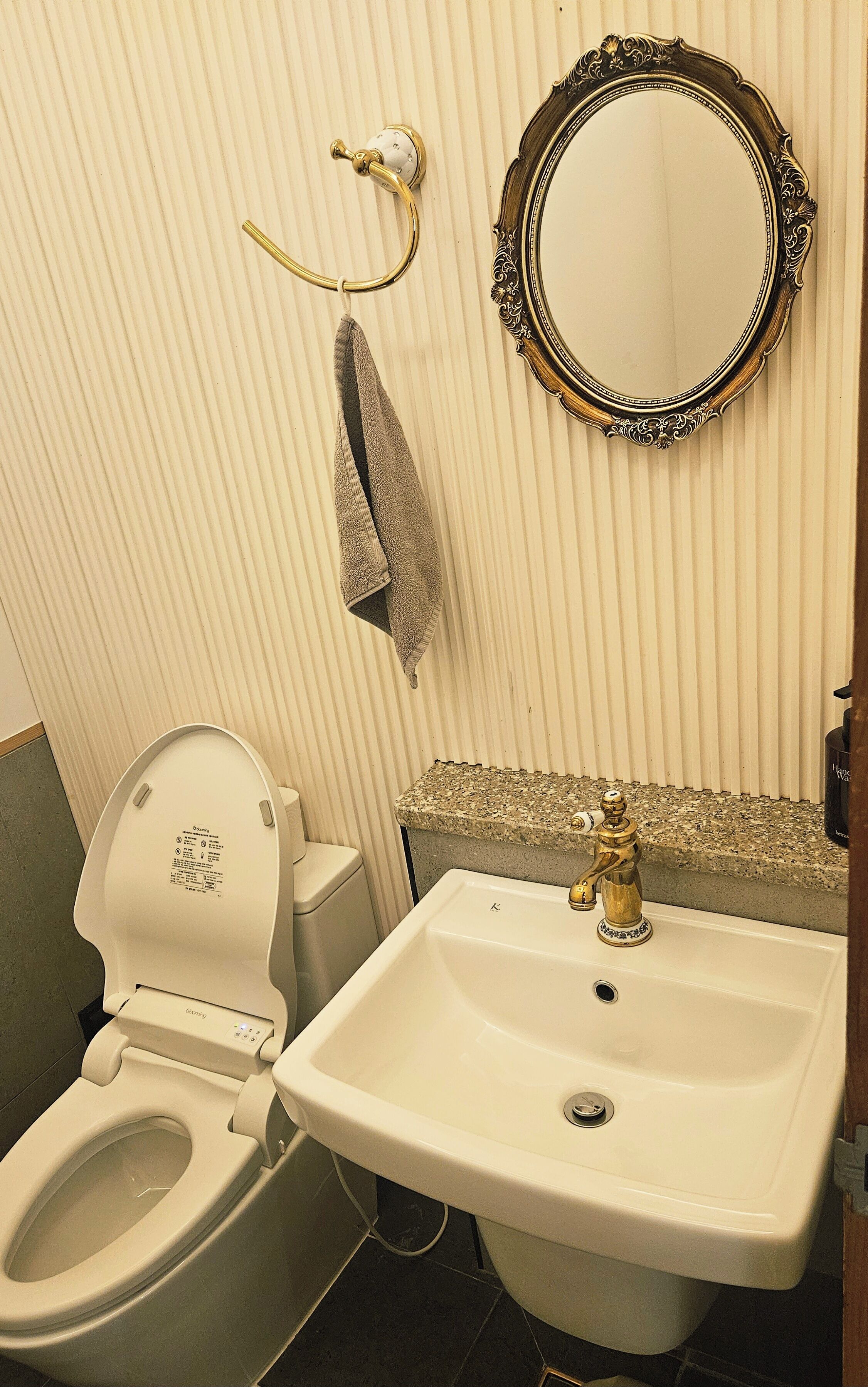 A bathroom with a toilet, sink, mirror, towel rack, and a decorative wall panel.