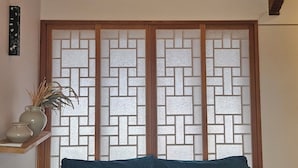 A room with a wooden ceiling, a ceiling fan, a green sofa, and a decorative partition with a geometric pattern. - Ohsudang Hanok Stay (Gyeongju)