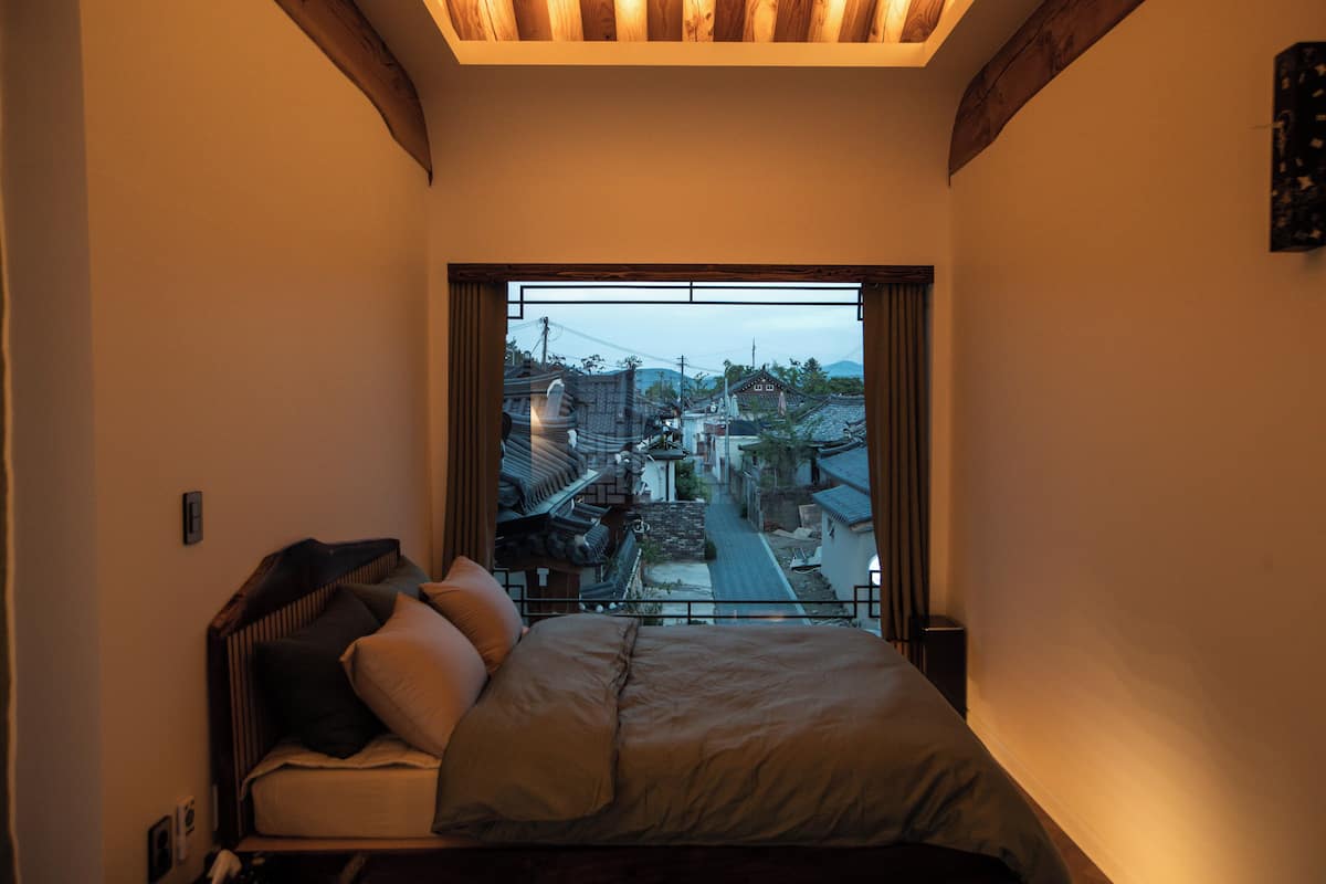 A bedroom with a bed, a window, and a view of a traditional village.