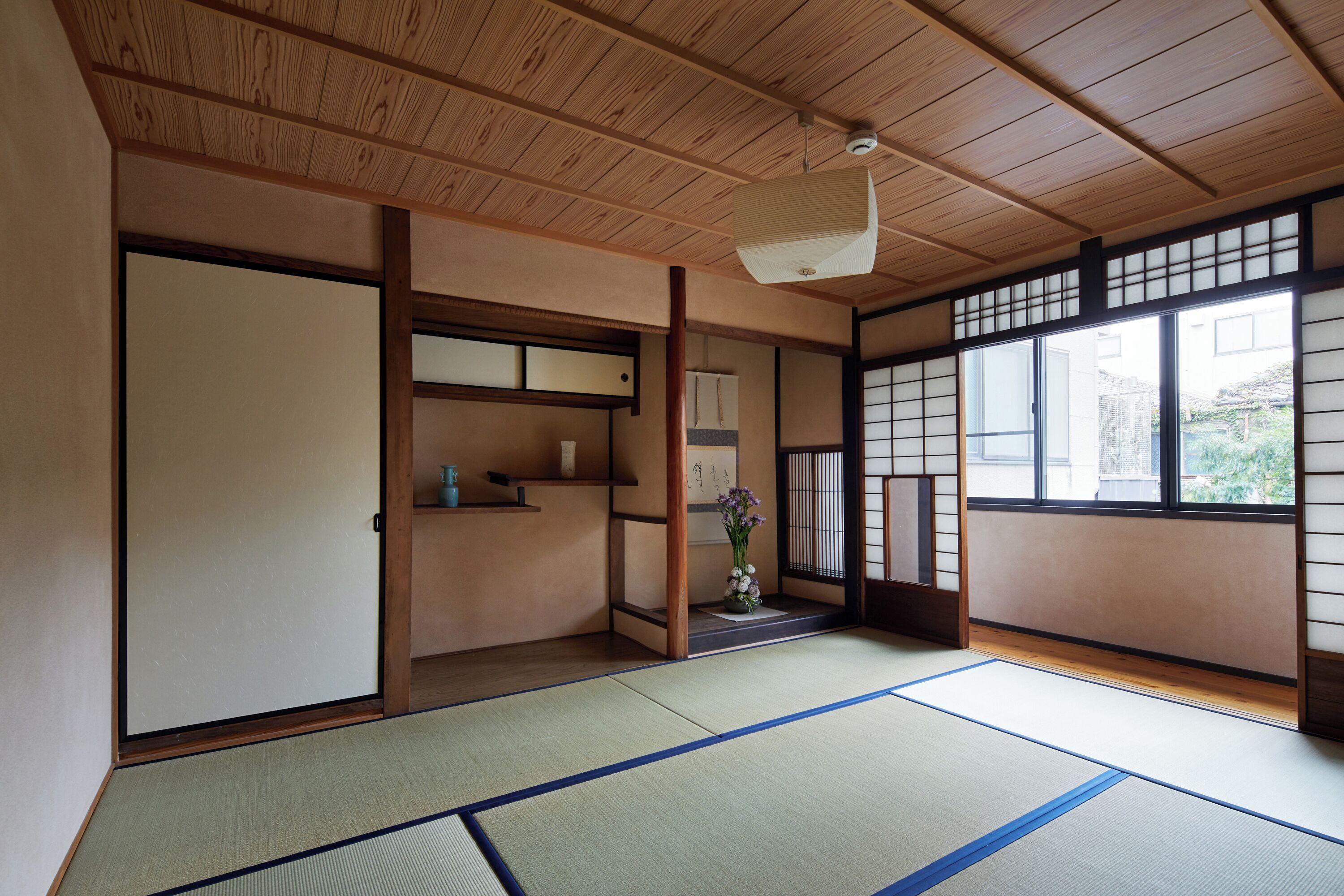 Una habitación japonesa tradicional con suelo de tatami, puertas correderas y vistas al exterior.