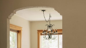 A dining area with a wooden table, black chairs, a chandelier, and a window with a plant on the sill.
