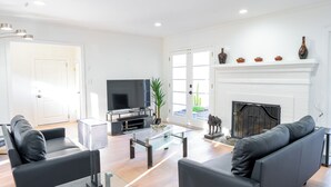 A modern living room with a flat-screen TV, two black sofas, a glass coffee table, and a fireplace. - Palo Alto Villa (East Palo Alto)