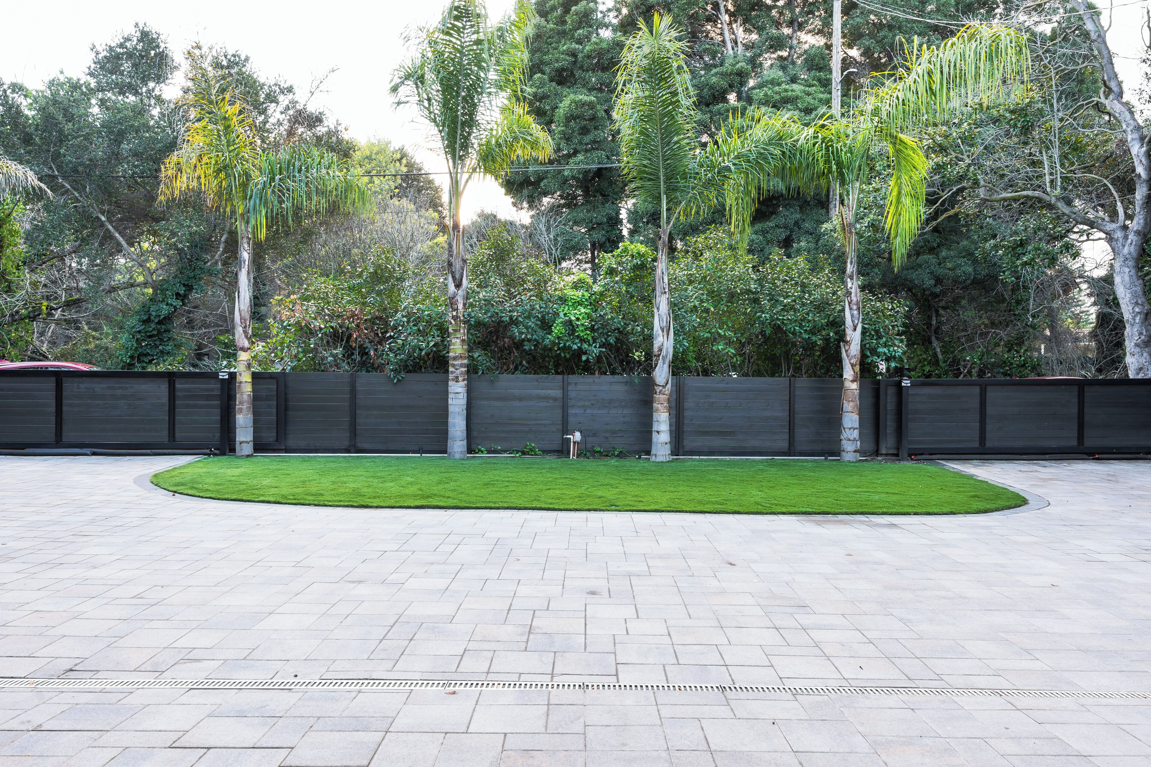 A paved courtyard with a central lawn, surrounded by a low wall and various trees.