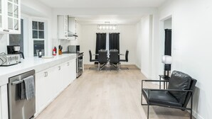 A modern kitchen with white cabinets, a dining area with a table and chairs, and a black leather chair. - Palo Alto Villa (East Palo Alto)