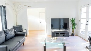 A modern living room with a black leather sofa, a glass coffee table, a flat-screen TV, and a potted plant. - Palo Alto Villa (East Palo Alto)