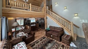A spacious living area with a high ceiling, wooden staircase, and a kitchen in the background. - 30 Mins from YNP -Trail Access-Three Little Bears (Island Park)