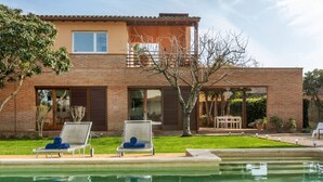 Una casa de dos pisos con piscina, dos sillones de descanso y un patio.