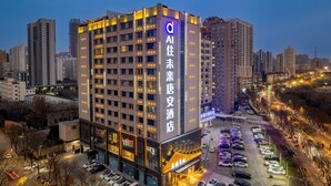 Un hotel de varios pisos con señalización iluminada, un estacionamiento y edificios urbanos aledaños.