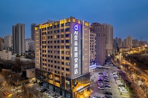 Un hotel de varios pisos con señalización iluminada, un estacionamiento y edificios urbanos aledaños.