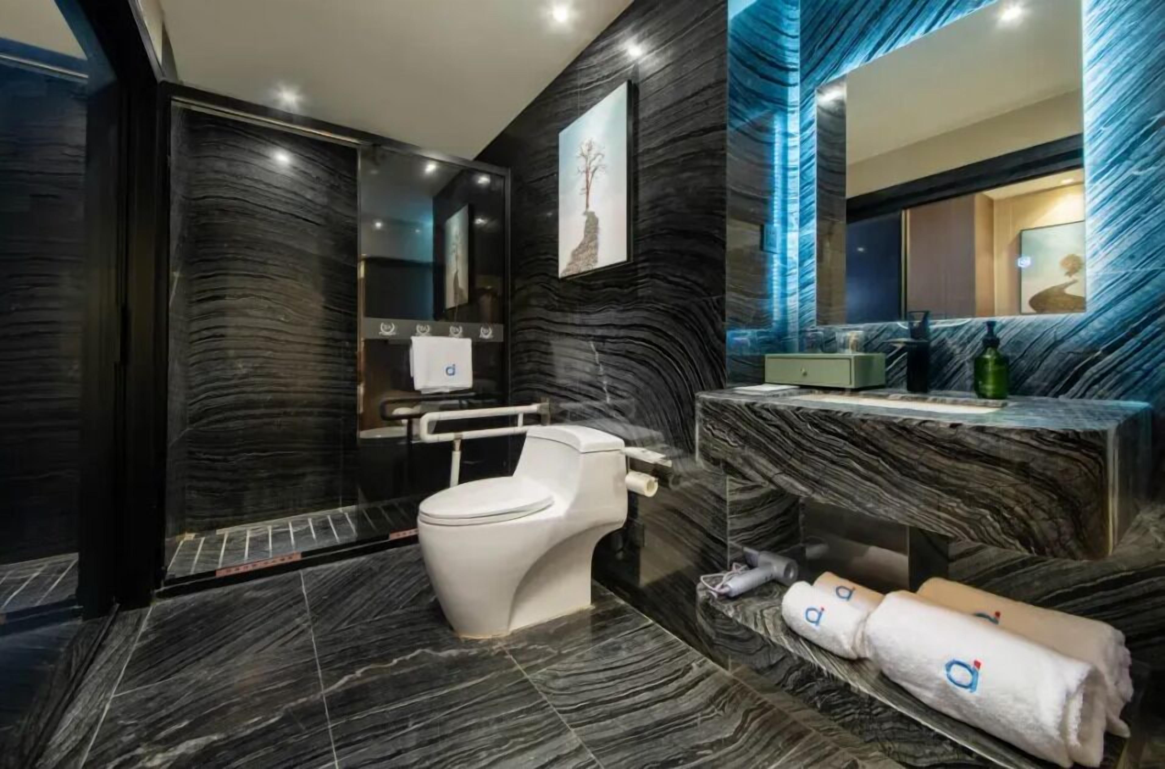 Un baño moderno con piso de mármol, inodoro blanco, tocador con espejo y un cuadro en la pared.