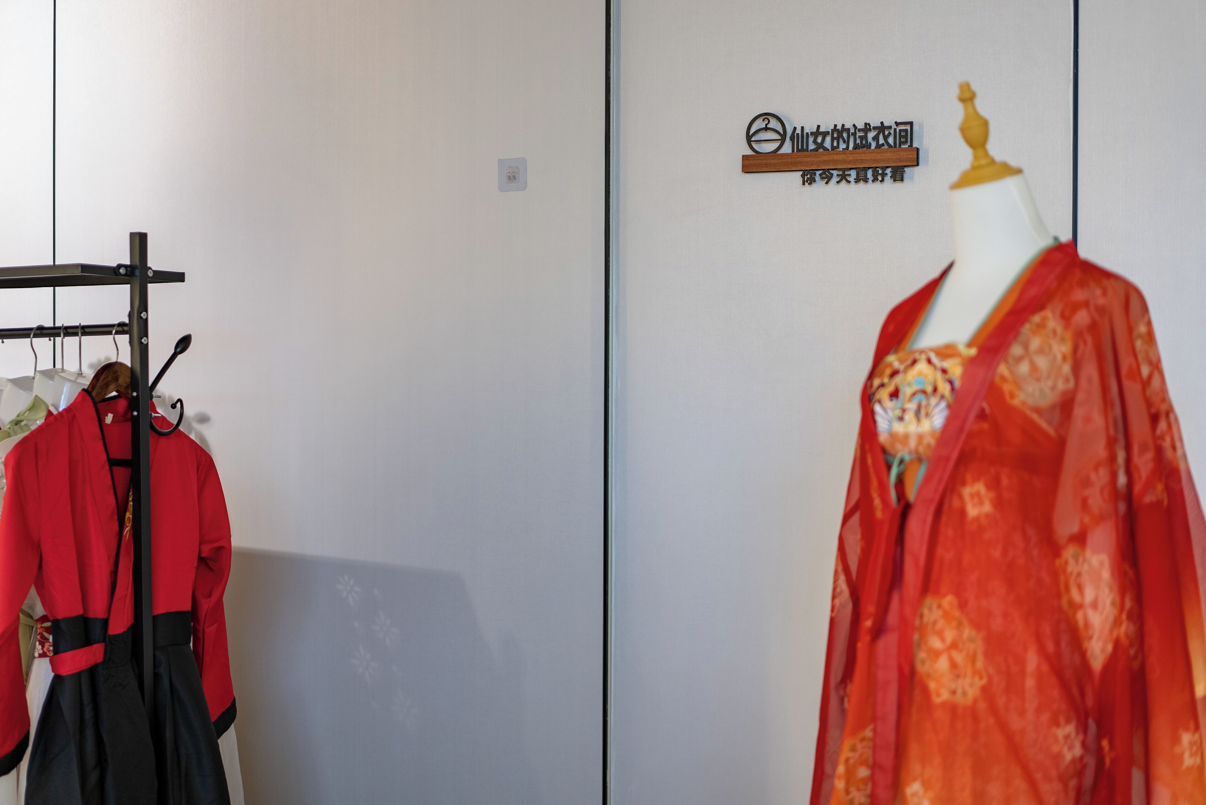 A mannequin in traditional attire, a rack with clothing, and a sign on the wall.