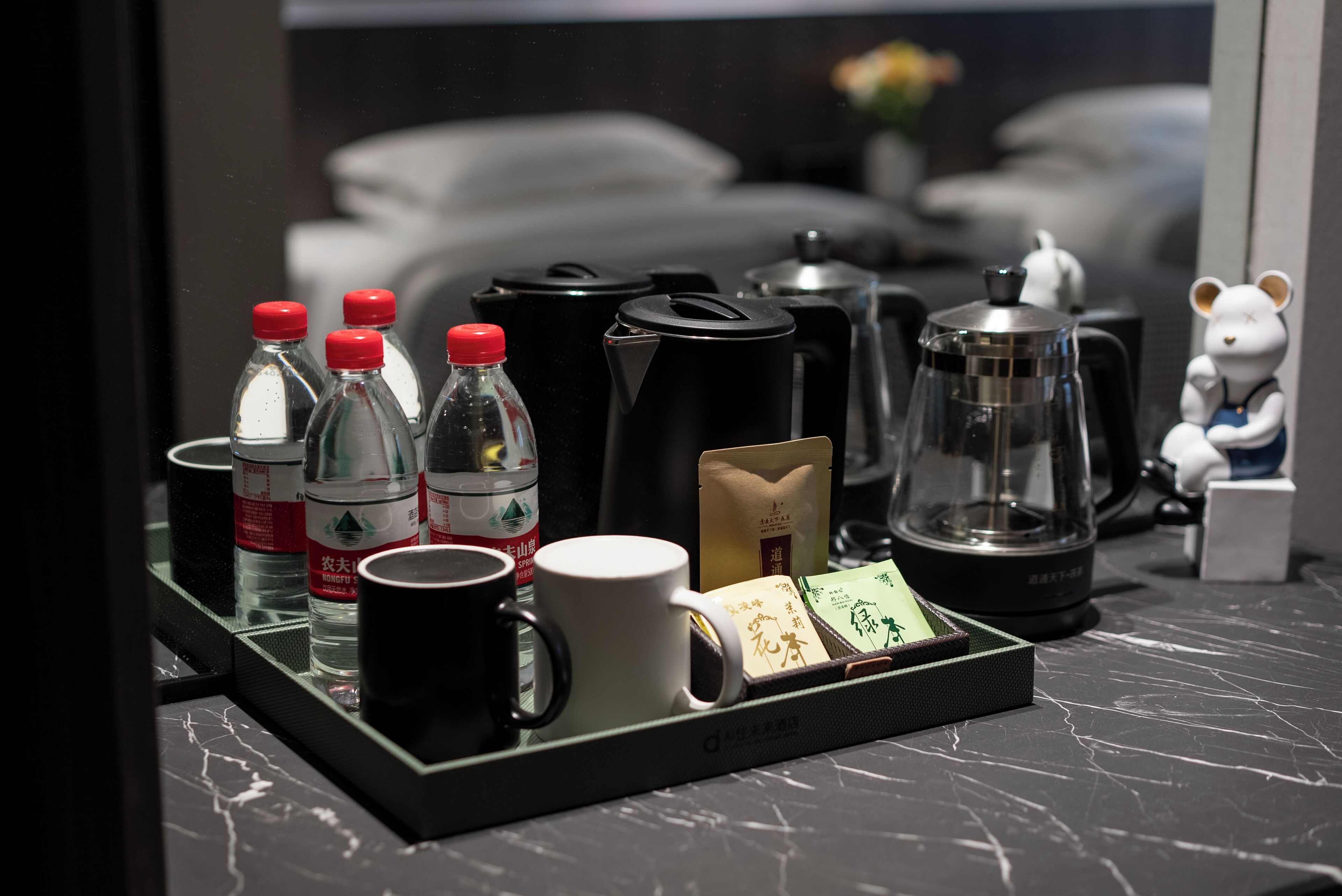En bakke med kaffemaskiner, flasker og en kop på en marmor bordplade.