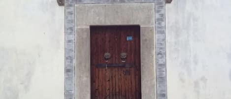 Puerta de madera con manija de metal, enmarcada en piedra, sobre un muro liso.
