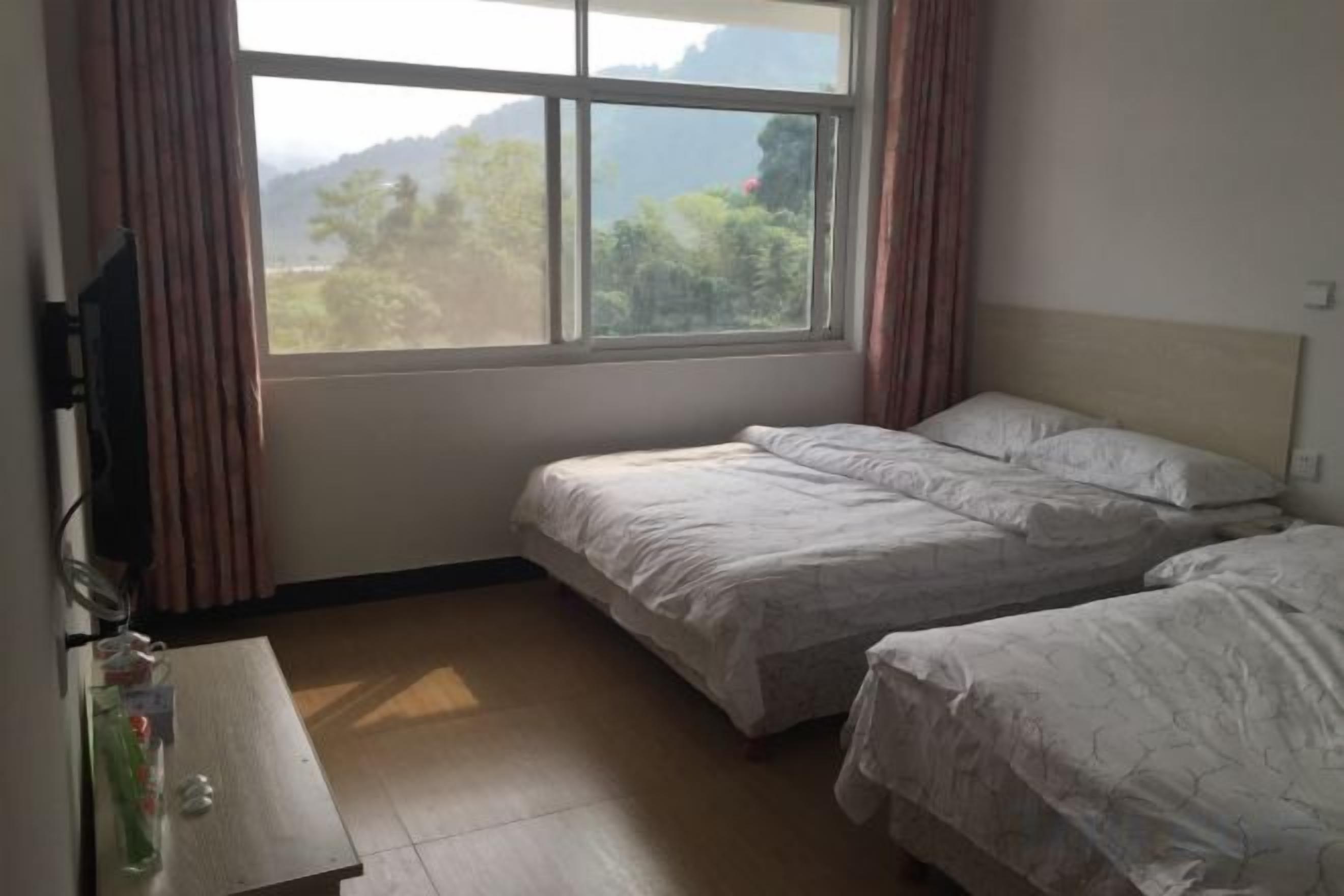 A room with two beds, a wooden desk, and a window with curtains.