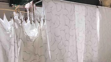 Ein Zimmer mit weißem Vorhang mit Blattmuster, einem Metallgestell mit Gegenständen und einer grünen Wand.