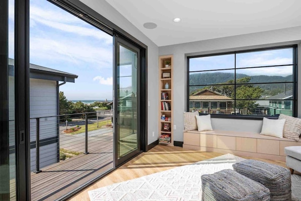 A modern living room with a large window, a bookshelf, a sofa, and a wooden floor.