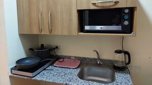 A compact kitchen with a microwave, a gas stove, a sink, and a kettle. - Florenze Khamsin Hurghada- - Room K203 (Hurghada 1)