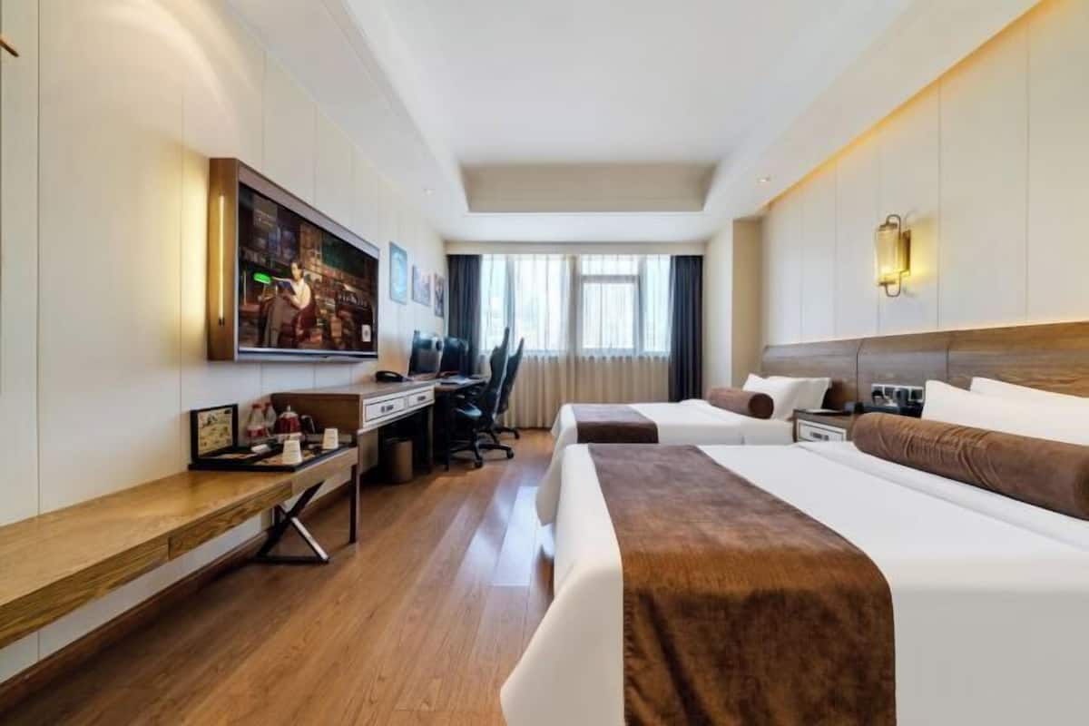 A hotel room with a bed, desk, chair, and a television on the wall.