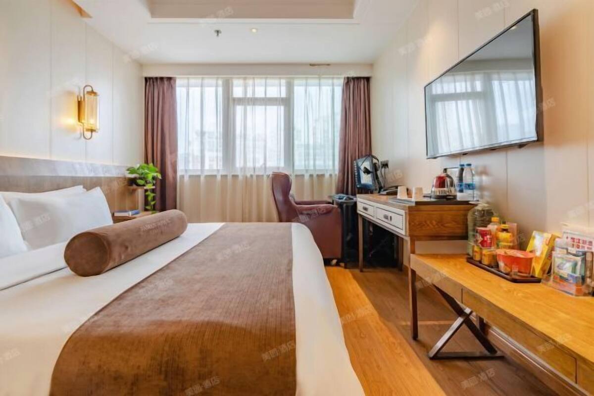 A hotel room with a bed, desk, chair, and a TV mounted on the wall.