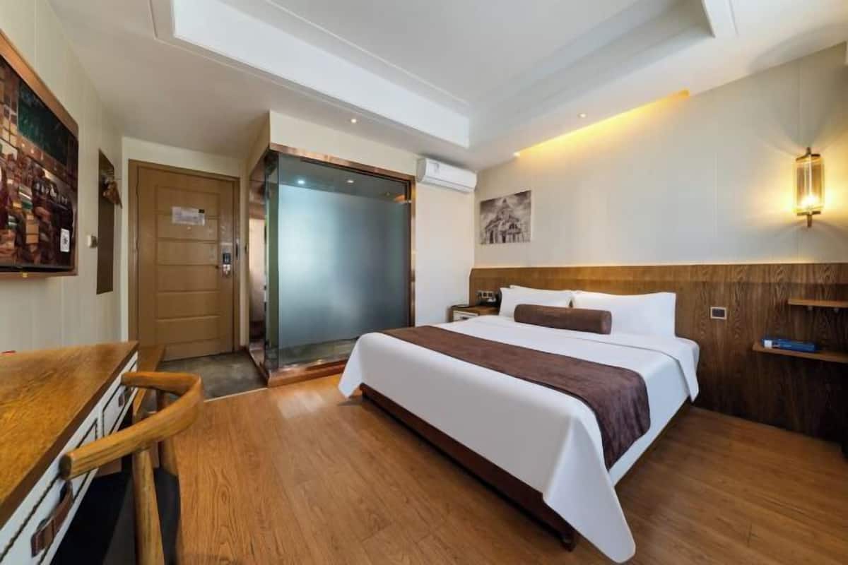 A hotel room with a large bed, a desk, a wardrobe, and a shower area.