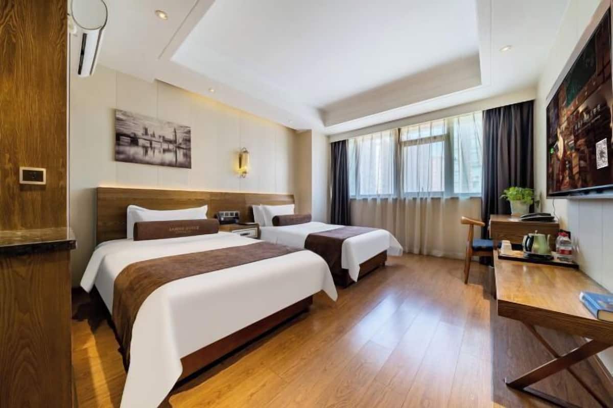 A hotel room with two beds, a desk, a chair, a TV, and a window with curtains.