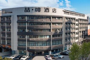 A multi-story hotel with a modern architectural design, featuring a central entrance and a parking area in front. - James Joyce Coffetel (Hefei Fortune Plaza, Haitang Metro Station) (Hefei)