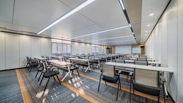 Une salle de conférence moderne, dotée de plusieurs tables et chaises, de grandes fenêtres et d’un sol recouvert de moquette.