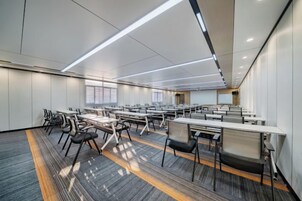 Una sala de conferencias moderna con varias mesas y sillas, ventanas amplias y piso alfombrado.