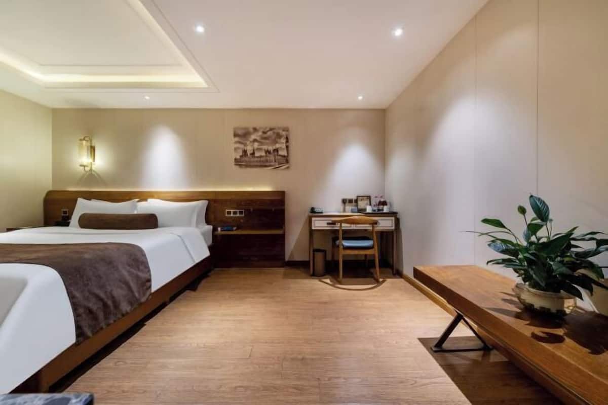 A hotel room with a bed, desk, chair, and a potted plant.