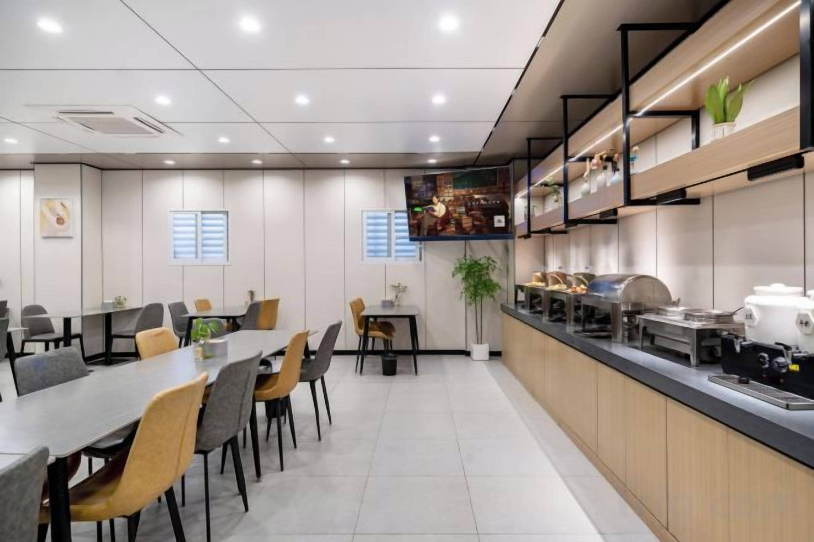 A modern dining area with tables and chairs, a kitchen counter, and a plant.