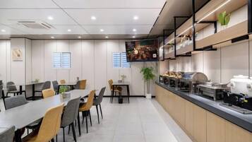 A modern dining area with tables and chairs, a kitchen counter, and a plant.
