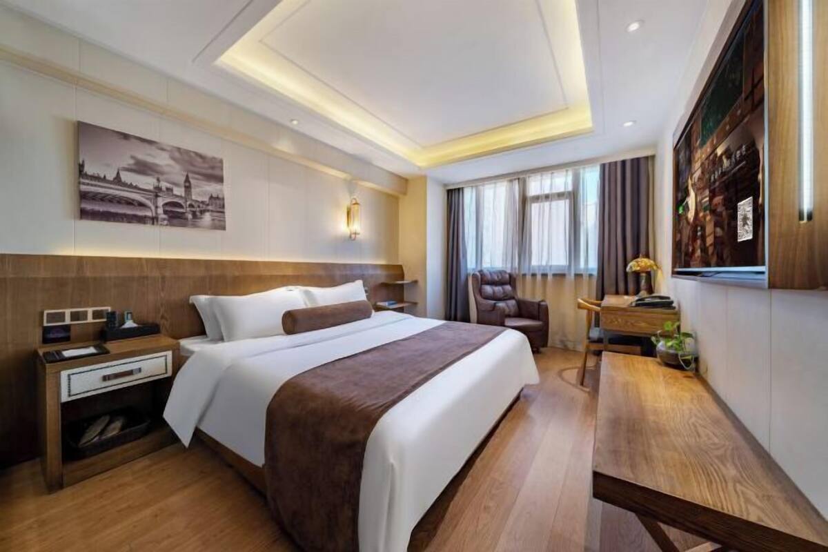 A hotel room with a large bed, a desk, a chair, and a wall-mounted TV.