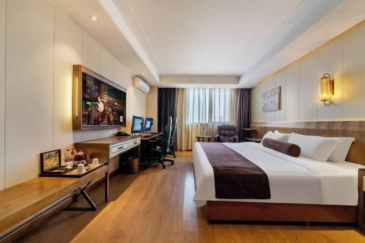 A hotel room with a large bed, a desk with a computer, a chair, and a television.