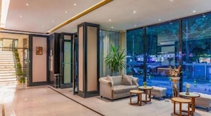 A modern hotel lobby with a sofa, coffee tables, and a large window offering a view of the street. - Xana Hotelle (Beijing)