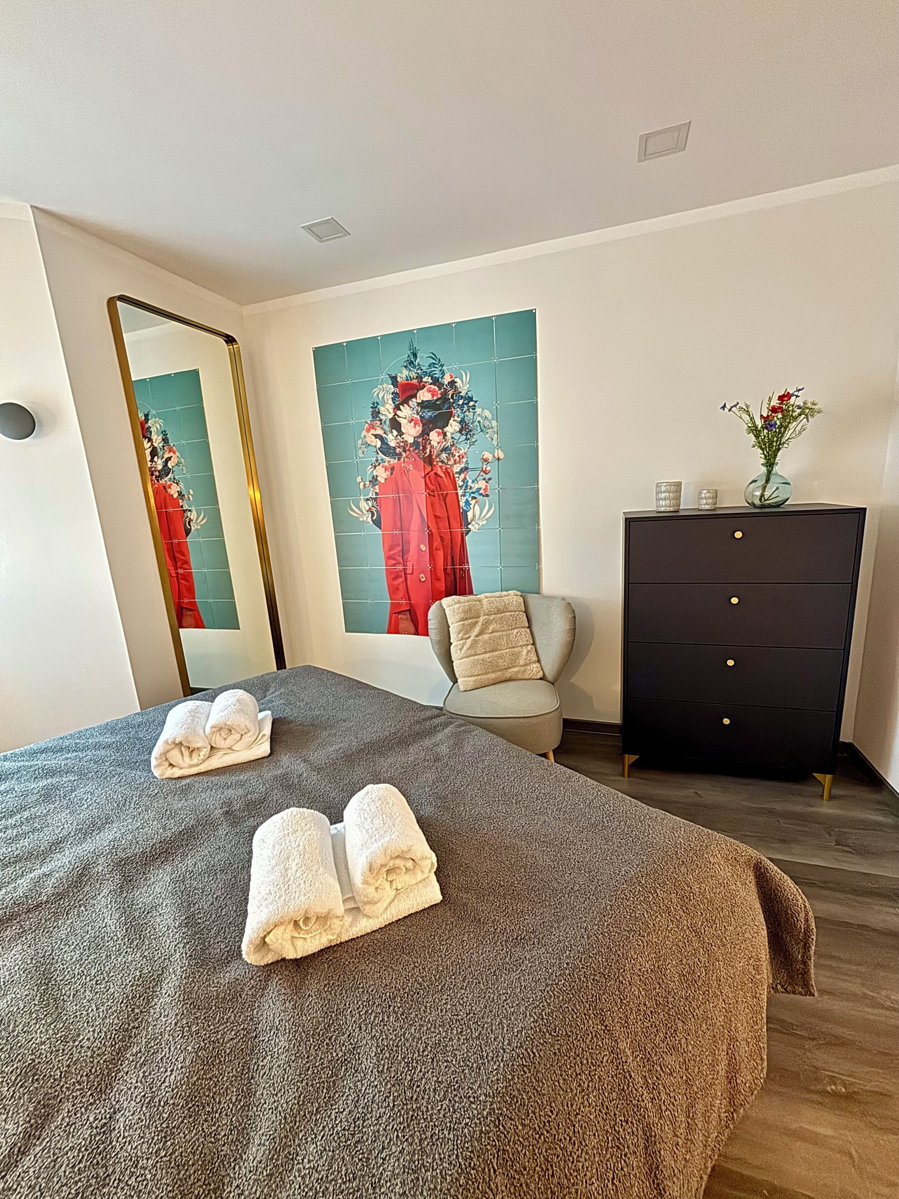 Une chambre d’hôtel avec un grand lit, une commode, une chaise et un miroir.